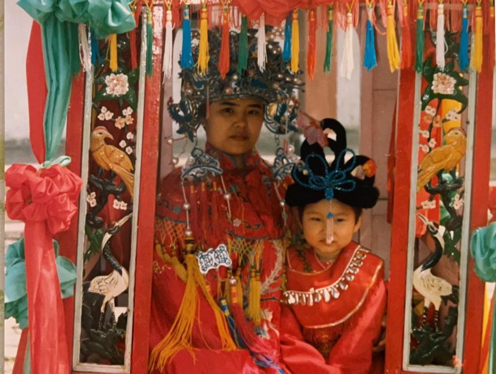 Yang as a child with her mother posing for photos in traditional attire. Red is considered a lucky colour in Chinese culture.